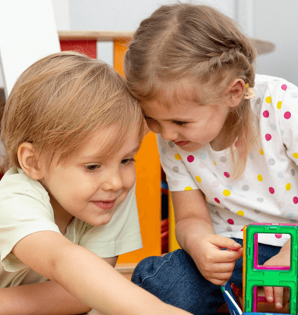 Two children playing with colorful magnetic blocks indoors.