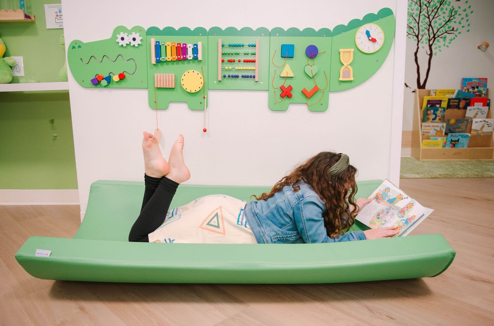 A little girl is laying on a green mat reading a book.