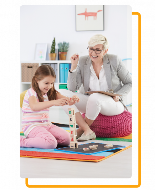 A therapist and a young girl stacking letter blocks during an ABA session.