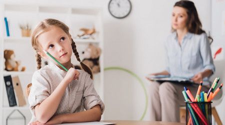 A little girl sitting at a table with a pencil in her hand