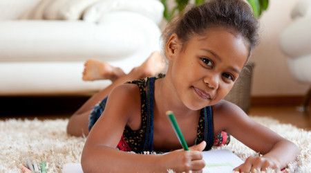 A little girl laying on the floor drawing with a pencil