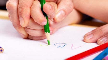 A person teaching a child how to write with a green pencil